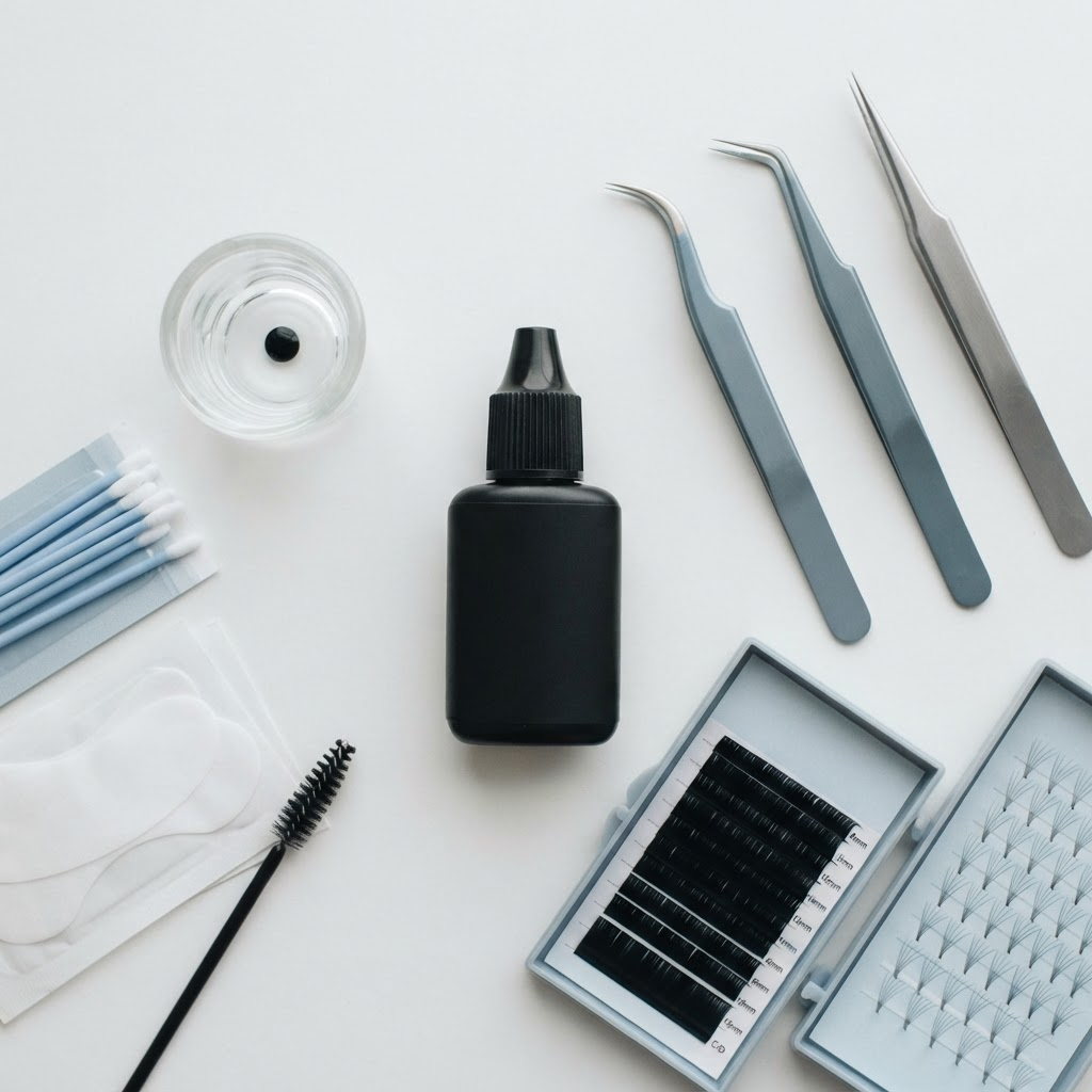 Professional lash extension adhesive bottle beside tweezers and lash trays on a clean workstation